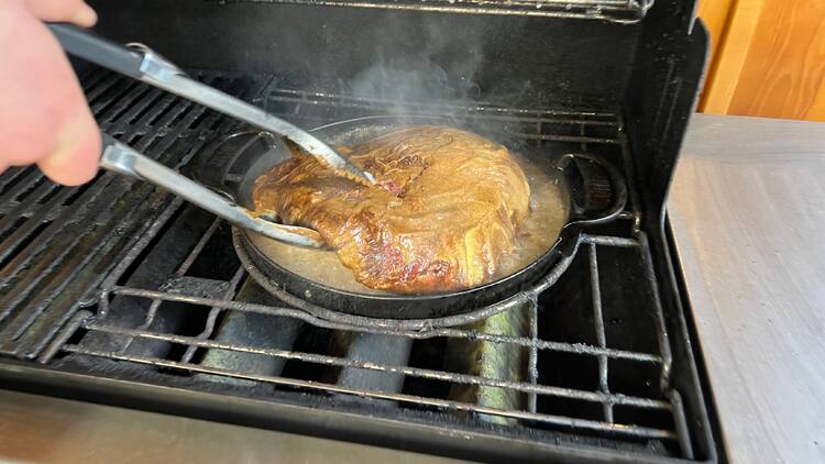 Grilmaster obrací maso kleštěmi v pánvi na grilu