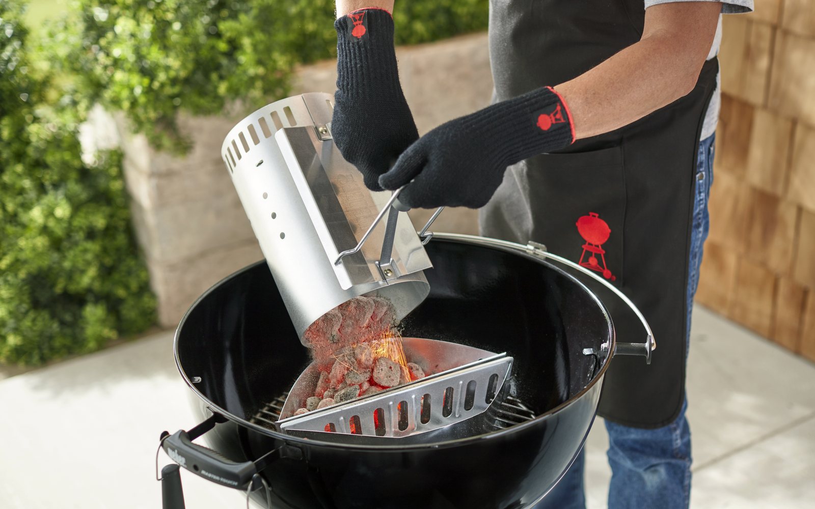 Vysypávání rozpáleného uhlí ze zapalovacího komínu do kotlového grilu v rukavicích