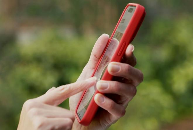 Ruce používají červený telefon v zahradě, pohled ze strany.